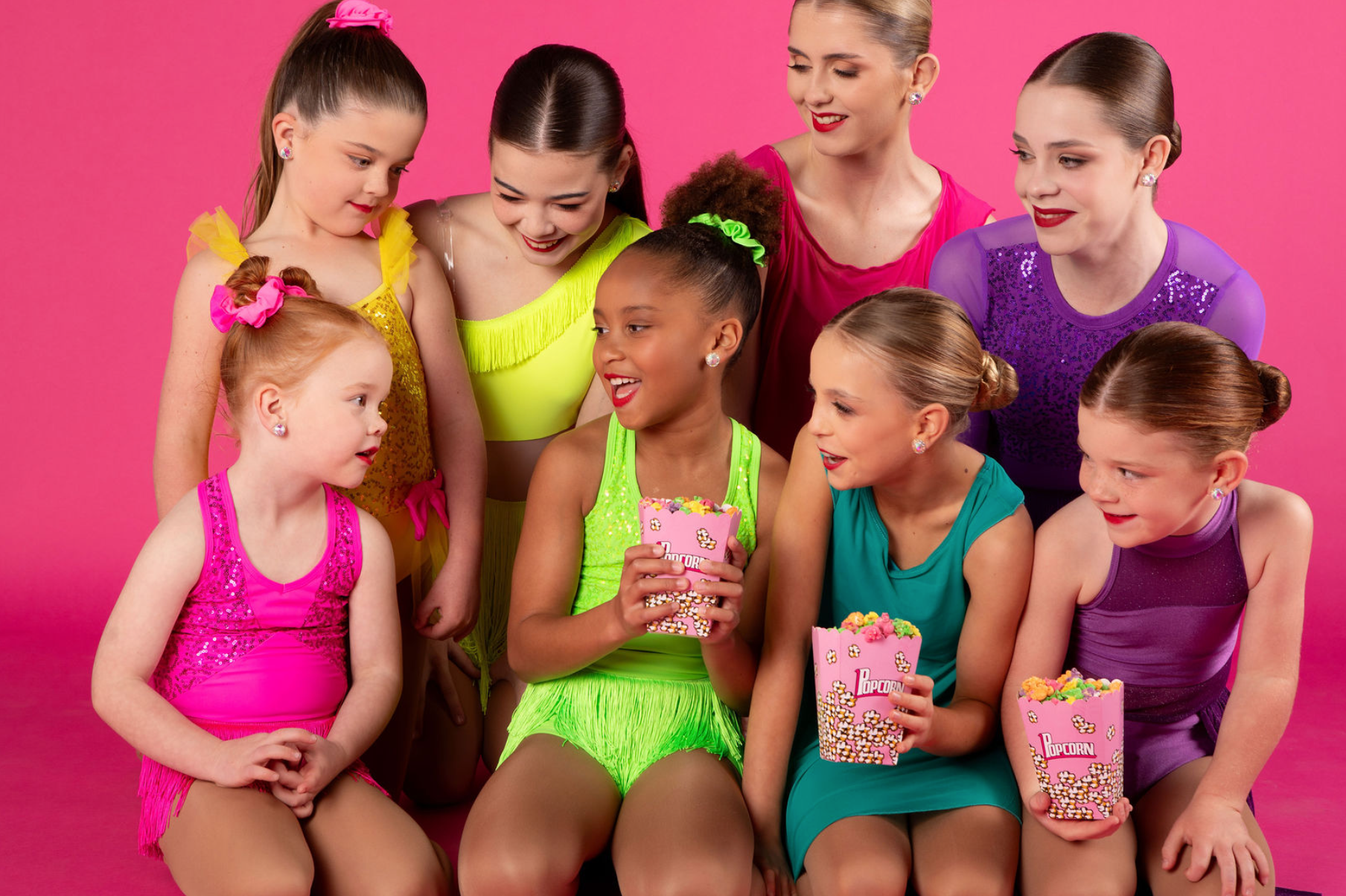 Group of young dancers in colorful outfits against a pink background